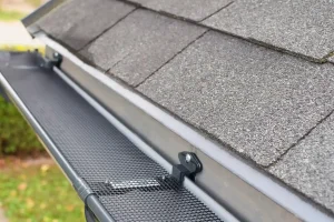 Close-up view of a roof with asphalt shingles and a metal mesh gutter guard installed to prevent debris from entering the gutter system.