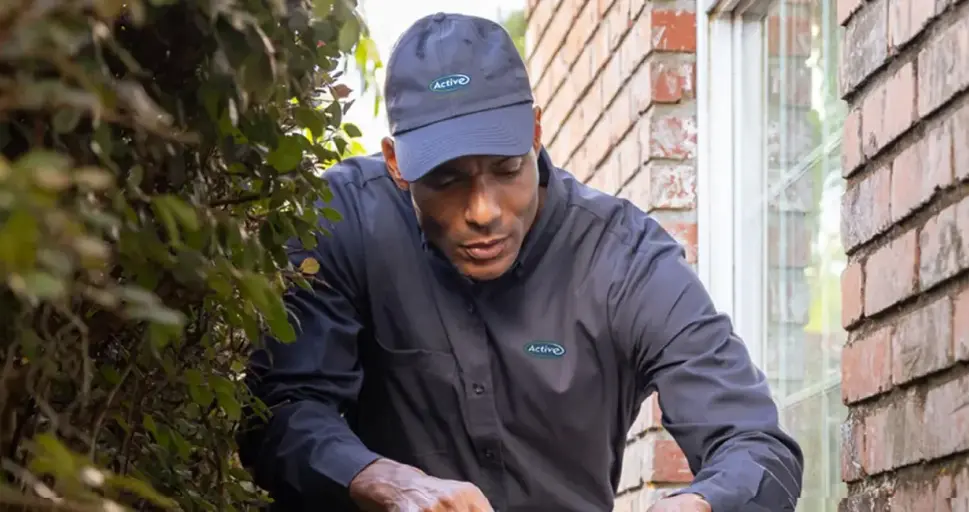 An Active Pest Control technician inspects a Georgia home's exterior foundation.