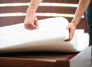Image of a man’s hands checking for bed bugs under a mattress.
