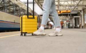 Image of the legs of a female walking with a yellow suitcase in a train station
