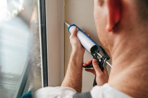 Image of a man using a sealant to seal the gap between a doorframe and the wall.