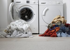 Image of two piles of laundry — one colored, one white – in front of two washing machines.