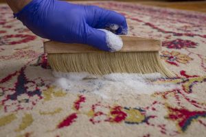 Hand with latex glove holding a brush, on a natural fiber rug with white foam, abstract texture,