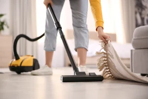 A woman picking up her rug to thoroughly vacuum her home for flea treatment.