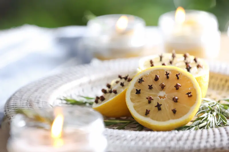 lemons-with-fresh-rosemary-on-plate Halved lemons studded with whole cloves on a white woven plate, surrounded by fresh rosemary sprigs and blurred burning candles in the background.